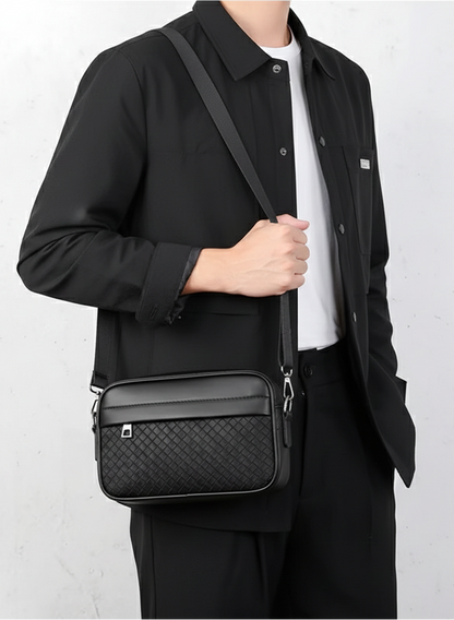 Person wearing a black jacket holding a black crossbody bag against a white background