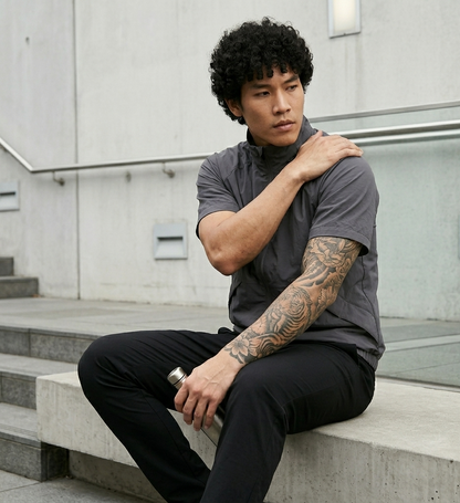 Man sitting on steps wearing a gray turtleneck and black pants, with tattoos visible on his arms.