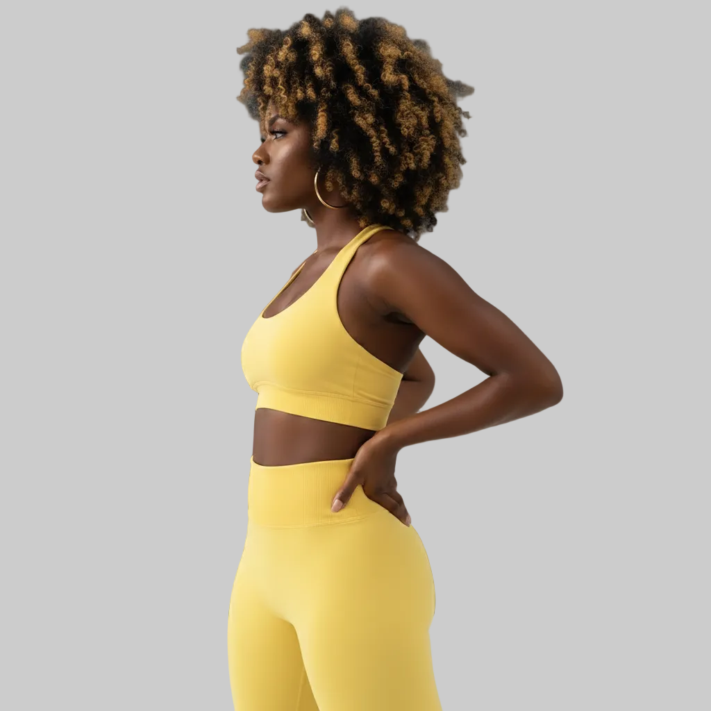 Woman wearing a yellow sports bra and leggings against a gray background