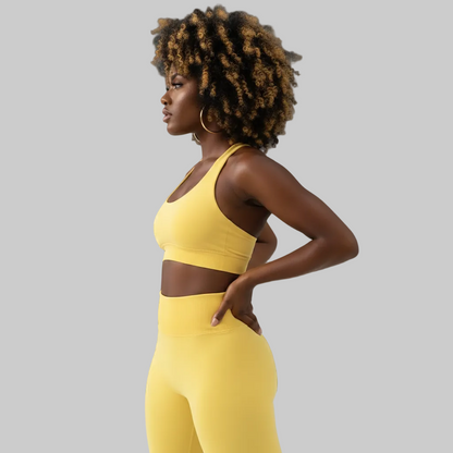 Woman wearing a yellow sports bra and leggings against a gray background