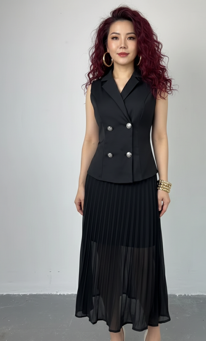 Woman wearing a black sleeveless blazer and pleated skirt against a plain background