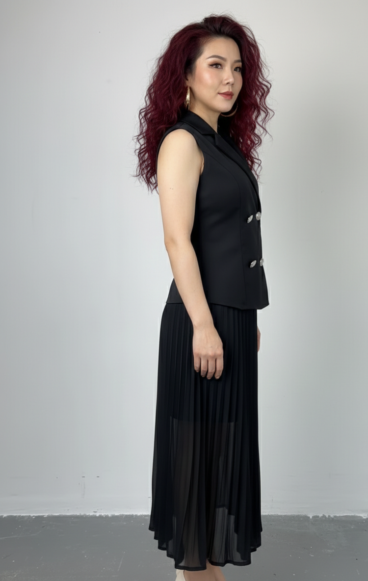 Woman wearing a black sleeveless top and pleated skirt against a plain background