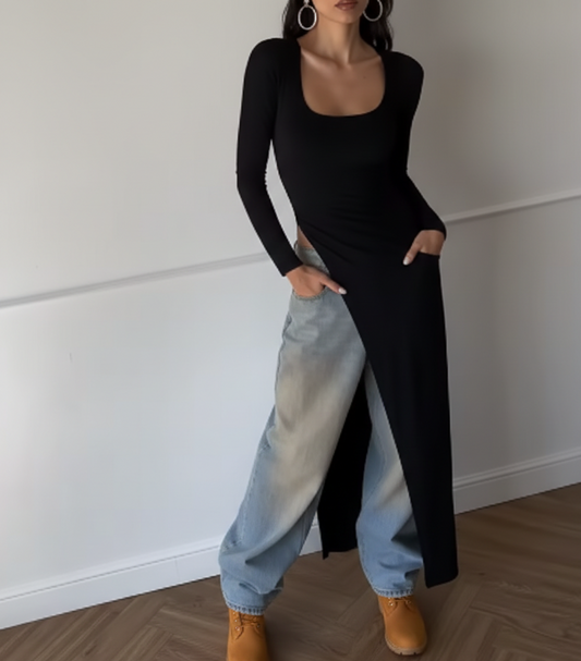 Person wearing a black long-sleeve top and light blue jeans with a white wall background