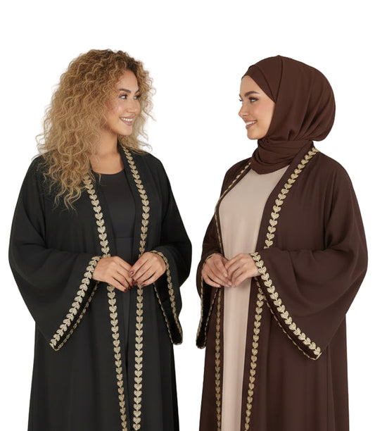 Two women wearing black and brown abayas with gold embroidery standing against a white background.