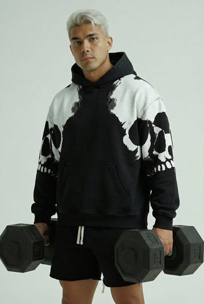 Person wearing a black and white skull-patterned hoodie holding dumbbells against a light gray background