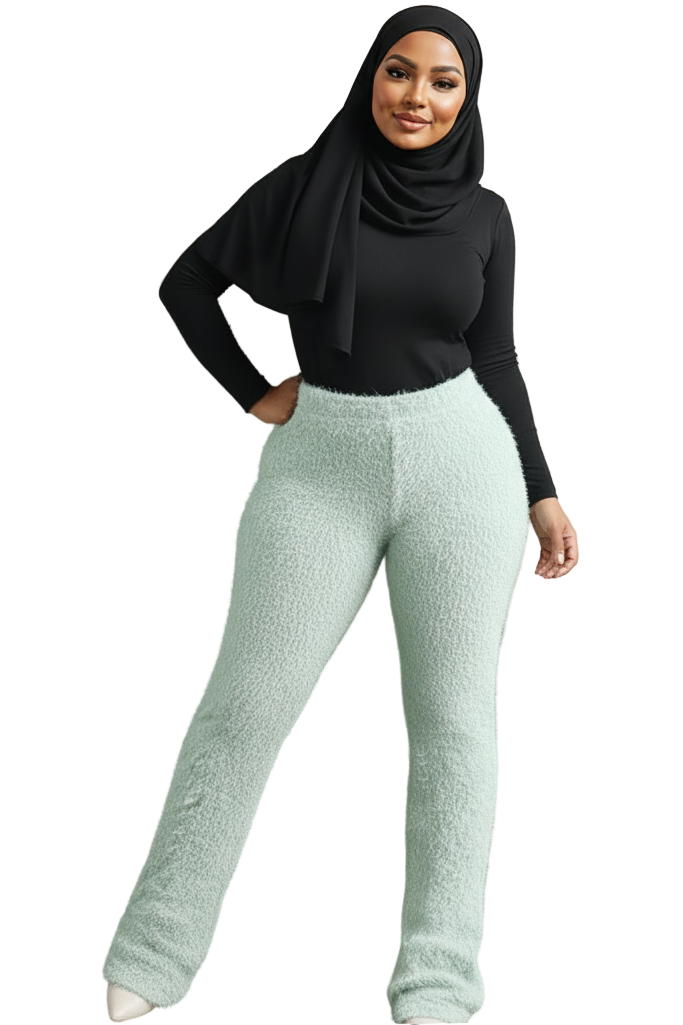 Woman wearing a black top and light green pants against a textured beige wall.