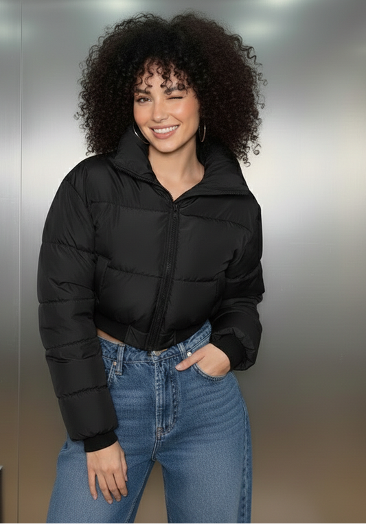 Woman wearing a black puffer jacket and blue jeans standing against a metallic wall.