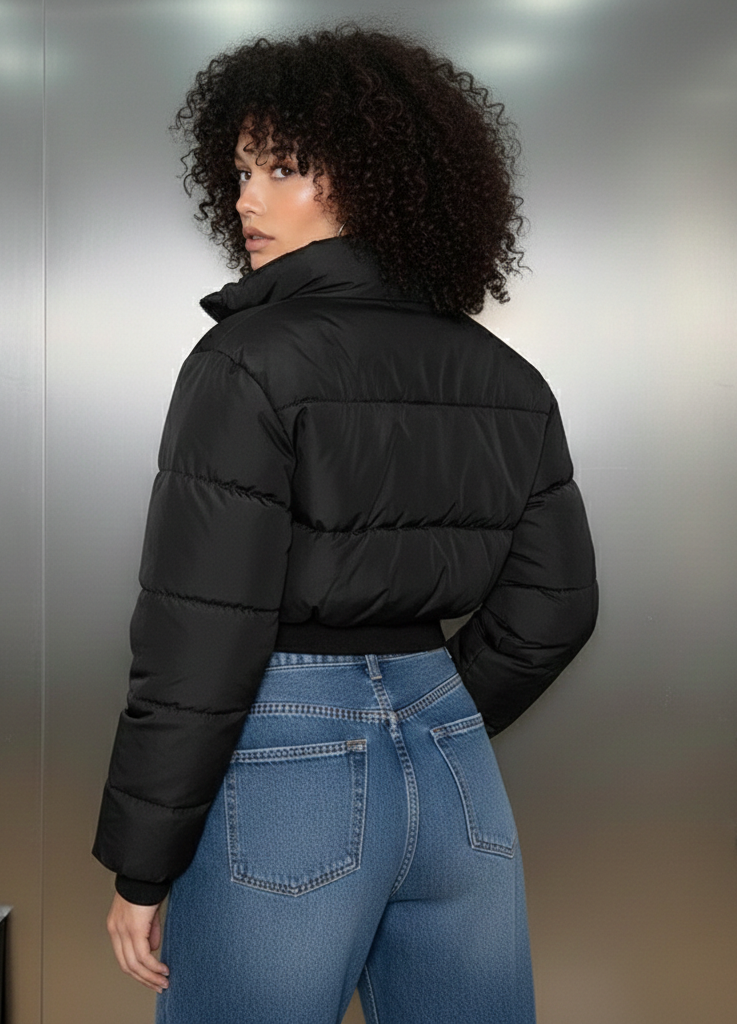 Person wearing a black puffer jacket and blue jeans standing against a metallic wall.