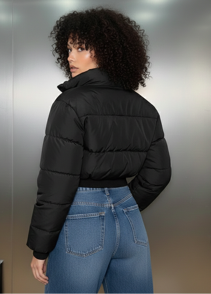 Person wearing a black puffer jacket and blue jeans standing against a metallic wall.