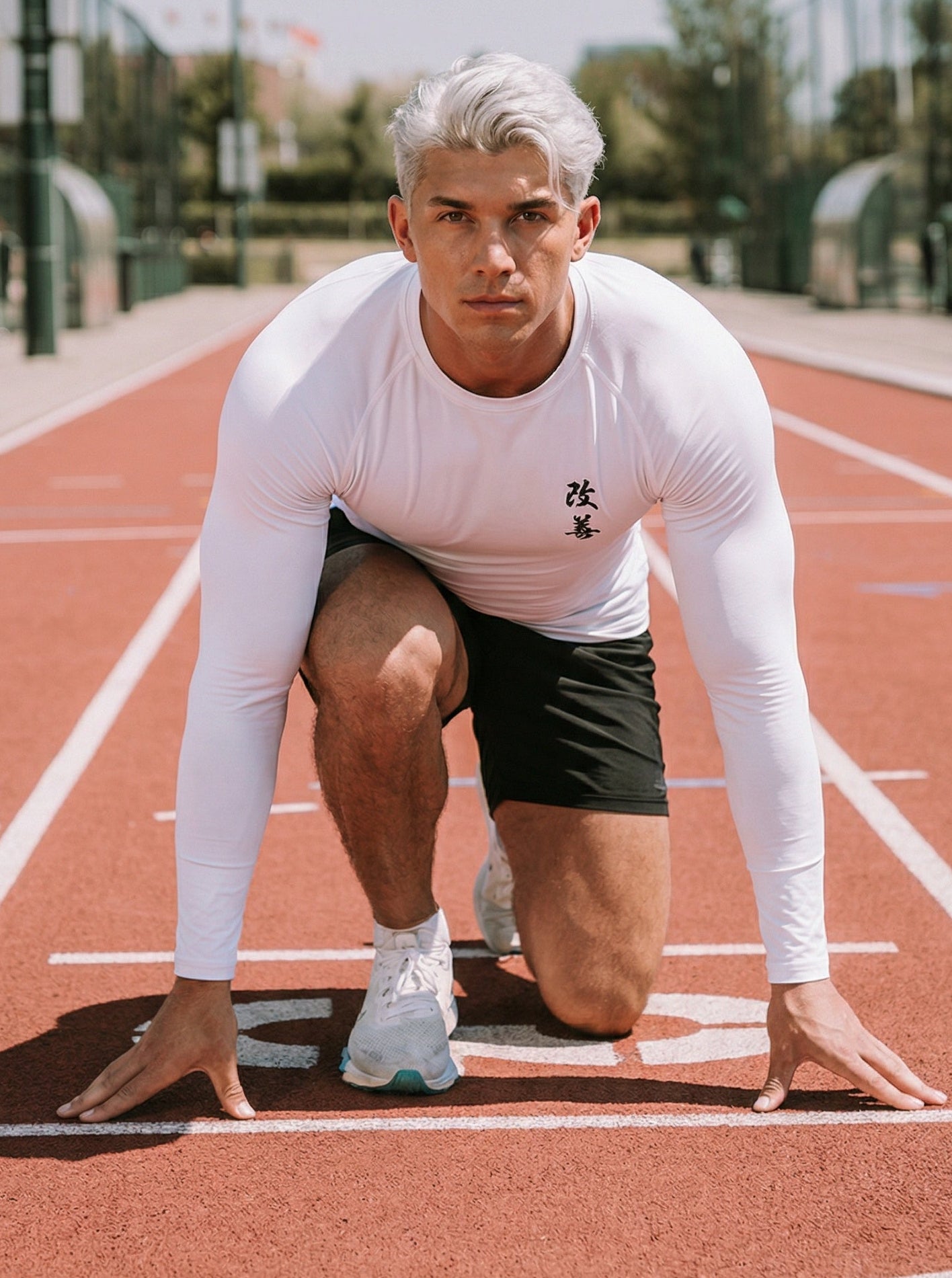 Athlete in white long-sleeve top and black shorts preparing to run on a track.