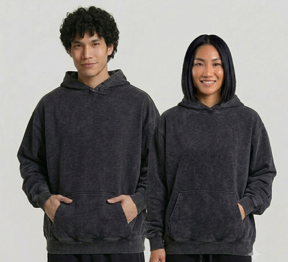 Two people wearing dark gray hoodies on a plain background