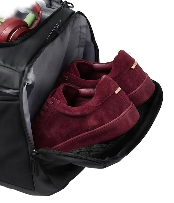 A black duffel bag shown open, with a pair of burgundy suede sneakers inside and red headphones partially visible in the top compartment, photographed on a white background.
